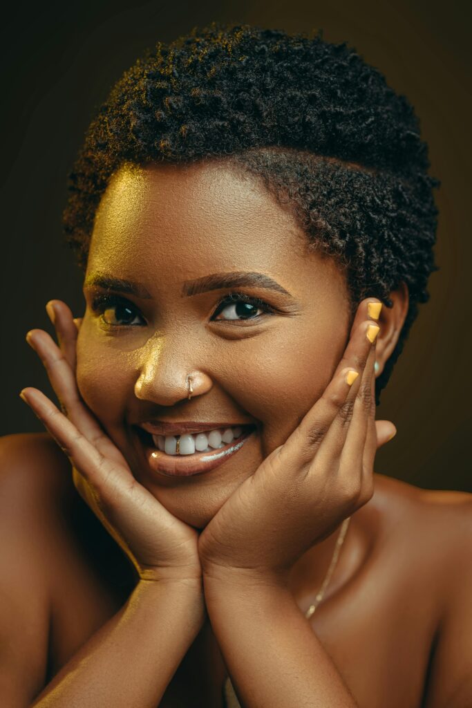 Close-up of a smiling Black woman with natural short hair in a studio setting.