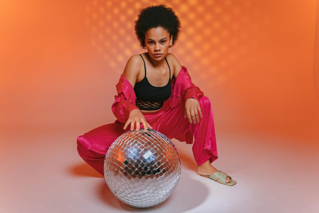 Confident woman in bright pink attire and afro hairstyle posing with a disco ball.